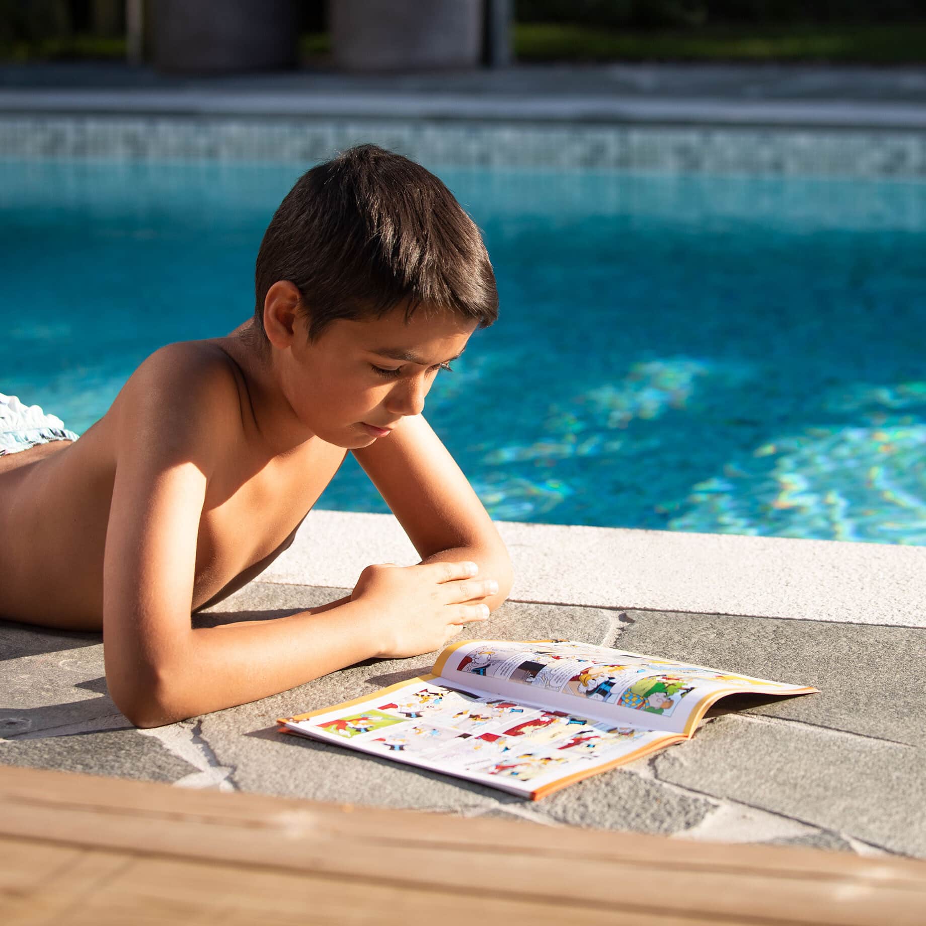 Pojke läser tidning på poolkanten